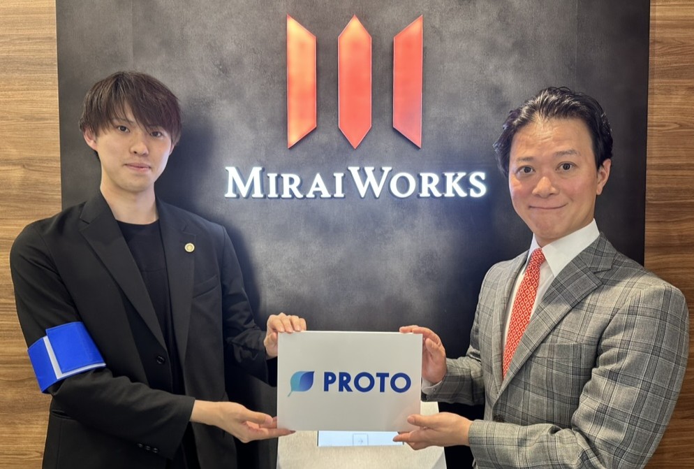 みらいワークス代表取締役社長の岡本祥治(右)と、ラジオ番組『PROTO』の又多弥羽(左)。みらいワークスのロゴを背景に、番組ロゴのボードを手に持つツーショット写真。